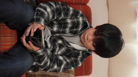 Vertical : Young asian boy playing online game with his smartphone on the sofa. Stock Footage 221379695