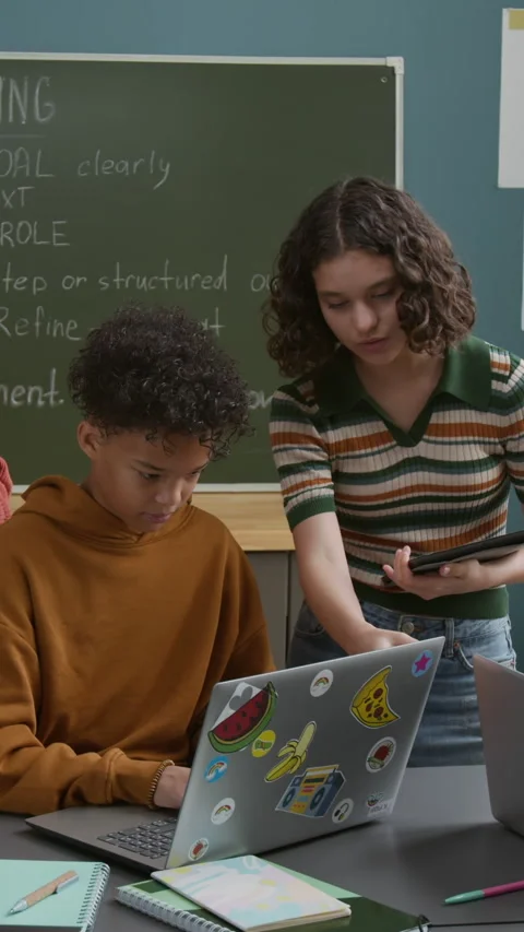 Vertical of Young Boy Working on Laptop in Classroom and Girl Helping Stock Footage 318729161