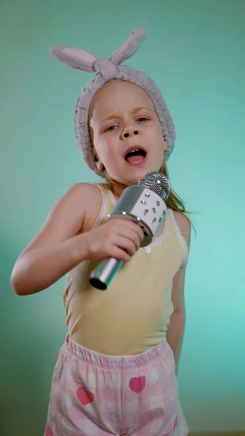 Vertical. Young child with bunny ears headband singing into a sparkling silver m Stock Footage 323373915