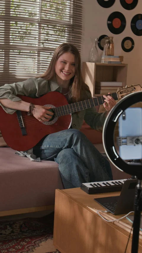 Vertical of Young Female Creator Playing Guitar while Filming Tutorial at Home Stock Footage 335409465
