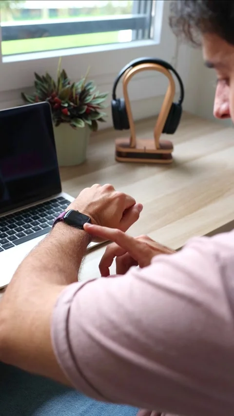 Vertical Young hispanic man using a smartwatch at his home office desk Stock Footage 319027706