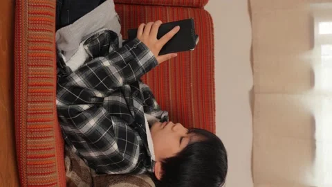 Vertical : Young kid playing online game with his smartphone on the sofa. Stock Footage 221379316