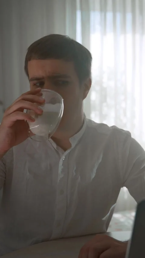Vertical of Young man drinks coffee in glass looking at screen of laptop Stock Footage 275640274