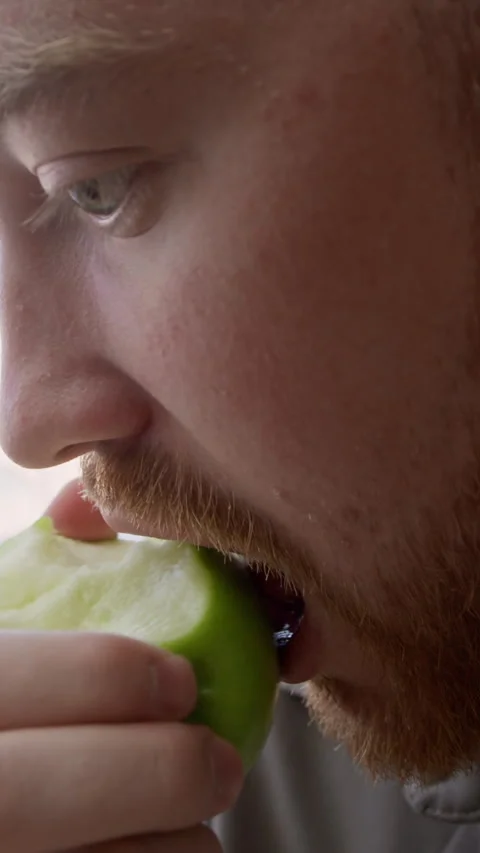 Vertical of Young Man Eating Green Apple while Working on Laptop at Home Stock Footage 315858587
