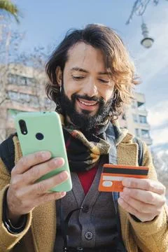 Vertical young man paying a purchase with a credit card and holding a smart Stock Photos