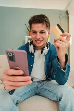 Vertical. Young man smiling while shopping online using a smart phone and credit Stock Photos