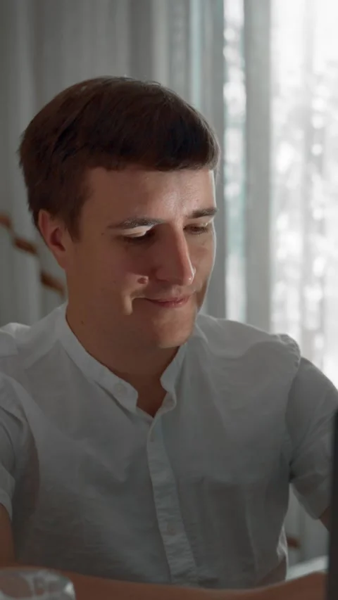 Vertical of Young man types article on laptop sitting at desk in kitchen Stock Footage 275640204