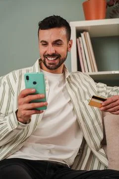 Vertical. Young man using his smartphone for online shopping, holding a cre.. Stock Photos