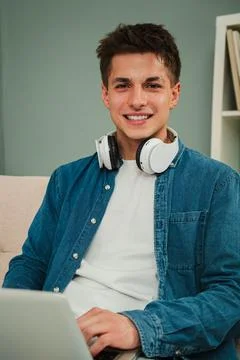 Vertical. Young man using laptop in cozy home living room, smiling confidently Stock Photos