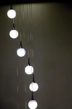 A vertically hanging lamp made of multiple round lights on a dark background Stock Photos
