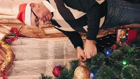 Vertically A man decorate a pine tree with beautiful balls for Christmas Stock Footage 143793767