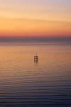 A vertically oriented view of a wooden structure in a calm sea at sunrise Stock Photos