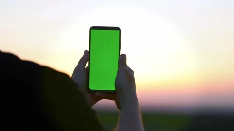 Vertically phone with a green screen in hands on a sunset background Video stock 194393318