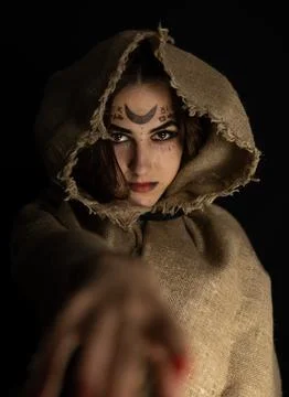 Vertically. Standing in the dim Halloween light, the witch holds out her hand to Stock Photos
