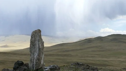 Vertically standing stone on a hilly plain against a rainy cloudy sky. Video stock 82221585