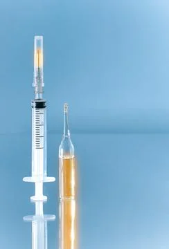 Vertically upwards directed syringe and ampoule with gold medicine. Stock Photos