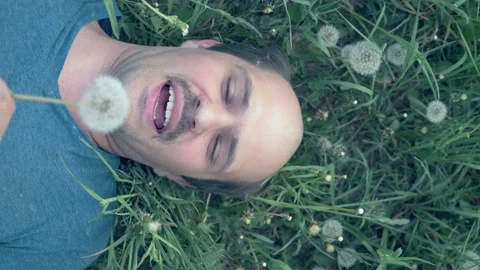 Vertically. a young balding man lying on the grass with dandelions and smiles Stock Footage 130910799