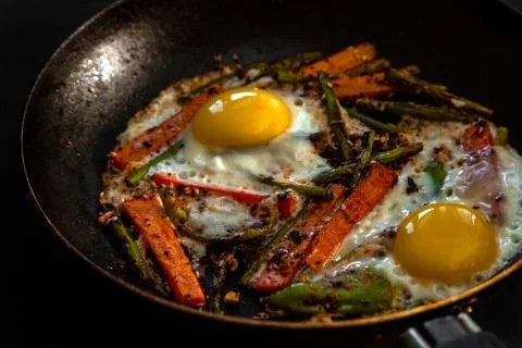 Very coarsely two fried eggs in a pan with large slices of carrots, bell peppers 写真素材