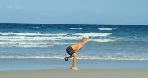A very fit young man doing Kettlebell Swings on a beach. Vídeo Stock 85511080