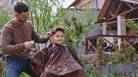 Very funny cute small boy have a haircut in the garden he make a cute face in Stock Footage 136196835