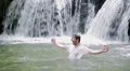 A very happy young man is celebrating in a river with a waterfall behind HD Footage
