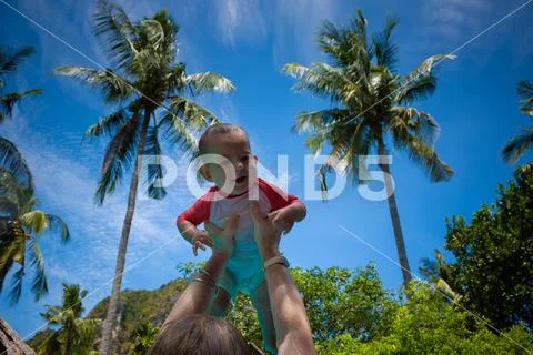 Very impressed baby little child raised high in arms against the sky and trop Stock Photos