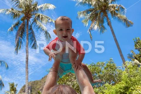 Very impressed baby little child raised high in arms against the sky and trop Stock Photos