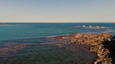 Very low drone flight over rocky foreshore at low tide with crystal clear calm 스톡 동영상 348113219