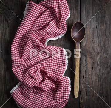 Very old empty wooden spoon and red kitchen towel on a brown wooden backgroun Stock Photos