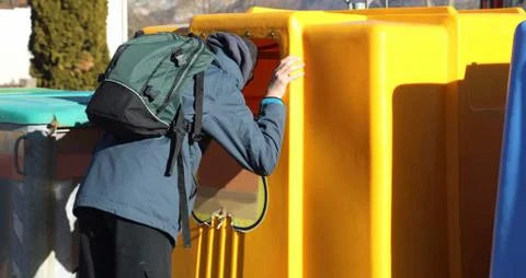 Very poor boy with a backpack on his back searching in the rubbish bin for so Foto stock