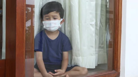 Very sad boy sitting behind window with face mask. Quarantine. Self-isolation. Stock Footage 162011433