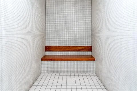 The very sober interior of a prison cell: bare tiled walls and a wooden bench Stock Photos