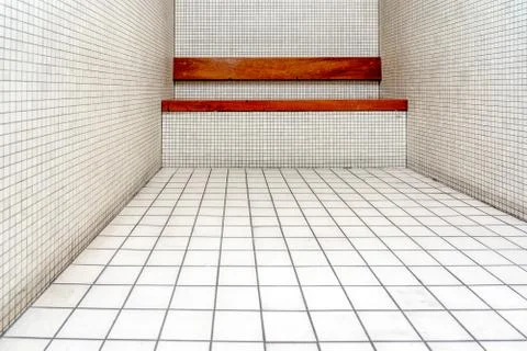 The very sober interior of a prison cell: bare tiled walls and a wooden bench Stock Photos