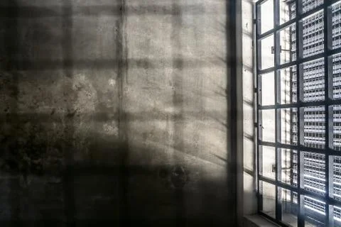 The very sober interior of a prison cell: barred windows with little light co Stock Photos