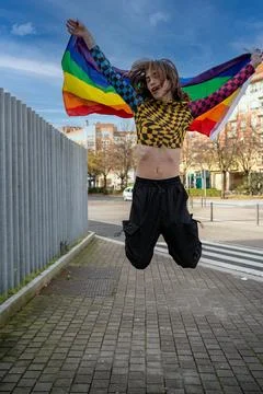 Very thin young man dressed brightly, jumping with the gay pride flag. Stock Photos