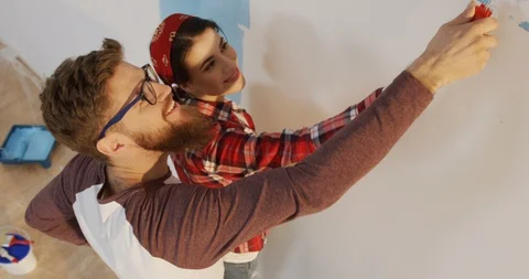 Vew from above on the hugging attractive couple painting a wall in blue with a Vídeo Stock 87587876