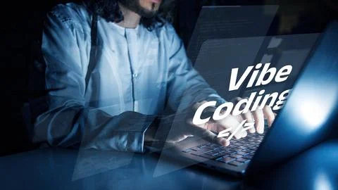 Vibe coding involves a person working on a laptop in a dimly lit room with a Stock Photos