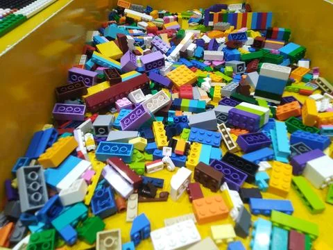 Vibrant assorted plastic building blocks fill a yellow bin, creating a joyful Stock Photos