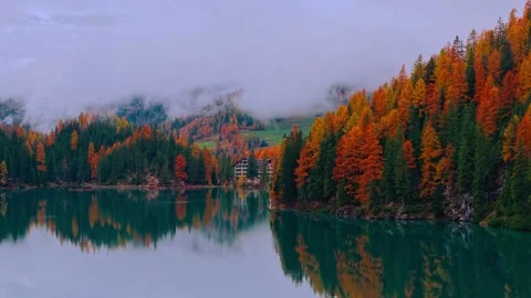 Vibrant autumn forest reflection on a calm mountain lake surrounded by low mist Stock Footage 340118287