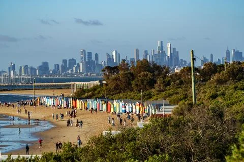 Vibrant bathing boxes line Brighton Beach, filled with people, overlooking .. Stock Photos