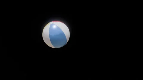 A vibrant beach ball is floating gracefully against a dark backdrop Video stock 287606309