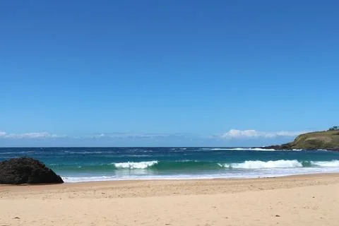 Vibrant beach view with rolling waves and clear skies during midday by the .. Foto stock