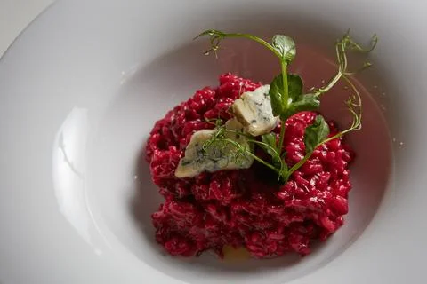 Vibrant beetroot risotto topped with blue cheese and microgreens in a white bowl Stock Photos