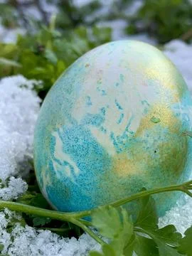 A vibrant blue and gold Easter egg is nestled in a patch of snow, surrounded by Stock Photos