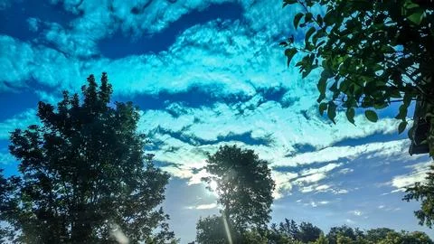 Vibrant blue sky with dramatic clouds and sunbeams filtering through green .. Foto stock