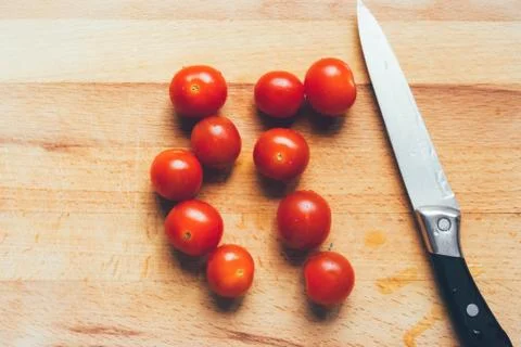Vibrant cherry tomato and kitchen knife on a wooden chopping board lying on g Stock Photos