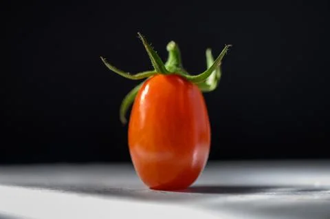 Vibrant cherry tomato resting on a white surface with dramatic lighting effec Stock Photos