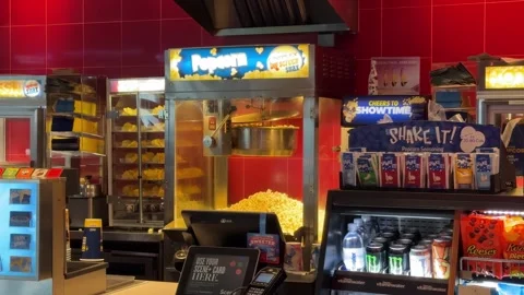A vibrant Cineplex concession stand showcases a large popcorn machine Stock Footage 313910836