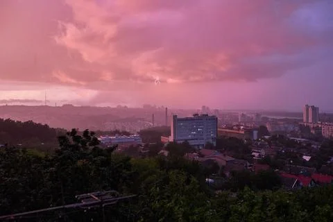 Vibrant city skyline under dramatic evening sky, lightning visible in distanc Stock Photos