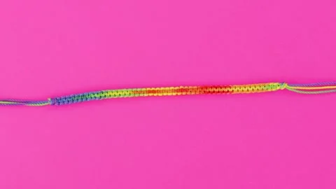 Vibrant close-up on threaded macrame bracelet, rainbow pattern set on pink Stock Footage 267820674